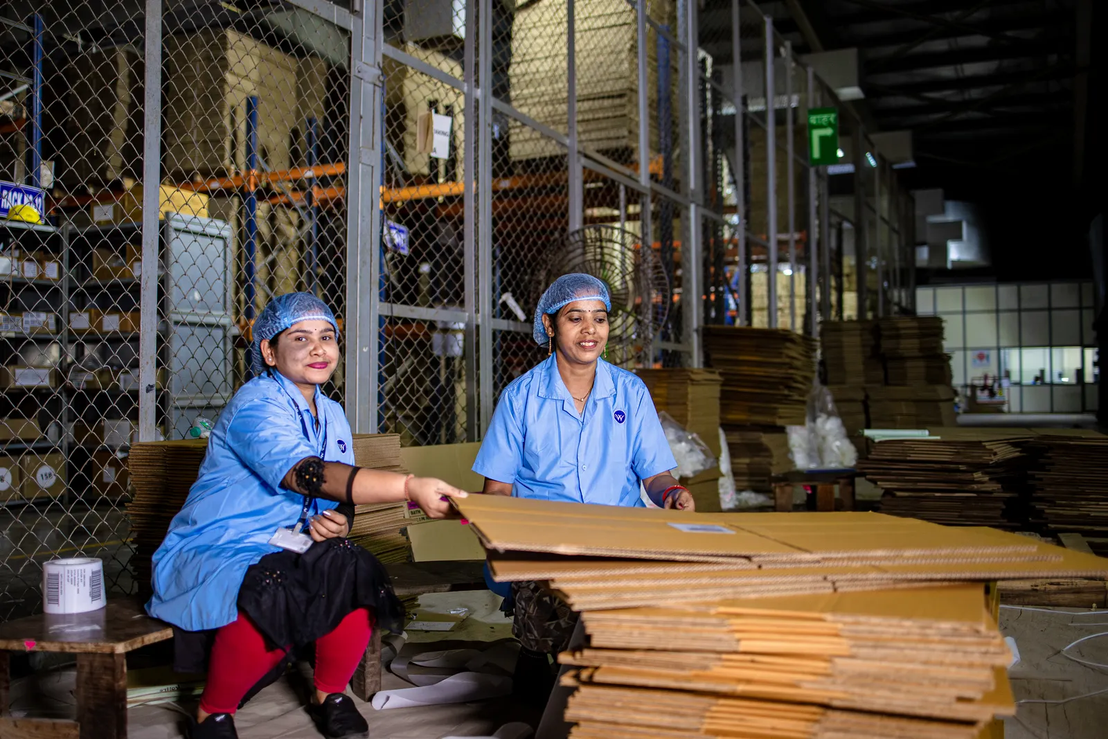 Two warehouse workers in uniforms handling cardboard stock in an industrial warehouse in India