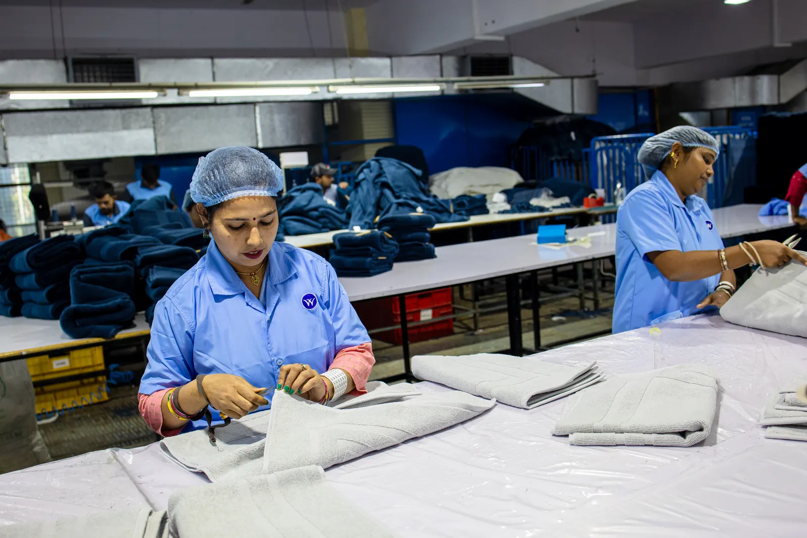 Production workers in uniforms and hair nets folding and checking finished goods on a factory line in India