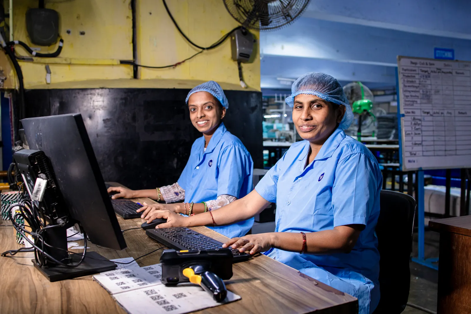 Two staff members in uniforms working at computer stations inside an Indian factory