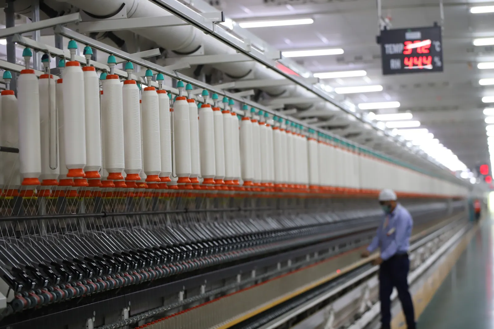 Long rows of spinning machines in a modern mill in New Delhi, with a worker walking the aisle